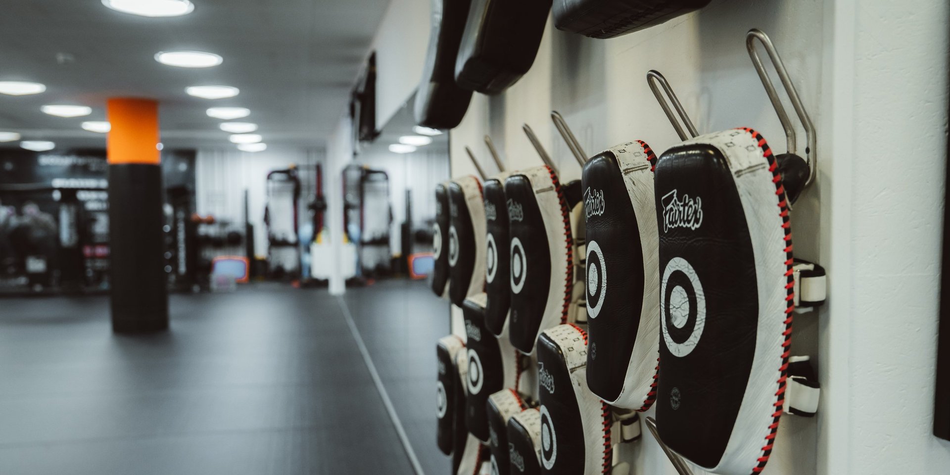 Row of black and white weight plates with red trim hanging on a gym wall with blurred fitness equipment in background