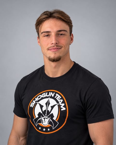 Young man with brown hair wearing a black Shogun Team graphic t-shirt against a gray background