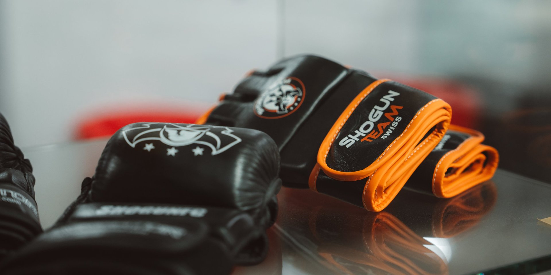 Black and orange boxing hand wraps and gloves arranged on a reflective surface