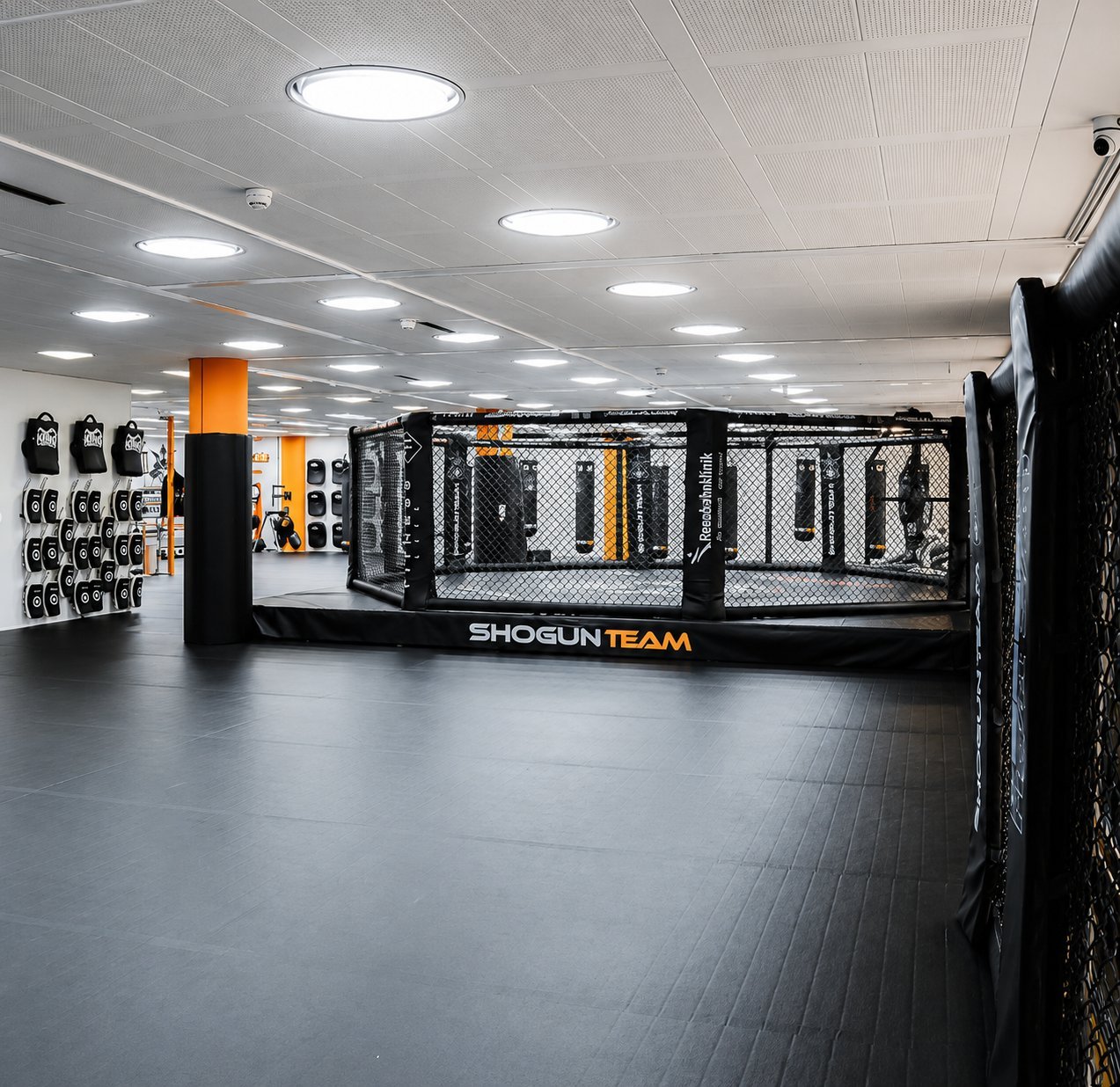 Interior of MMA training facility with Shogun Team octagon cage, equipment racks, and orange punching bag